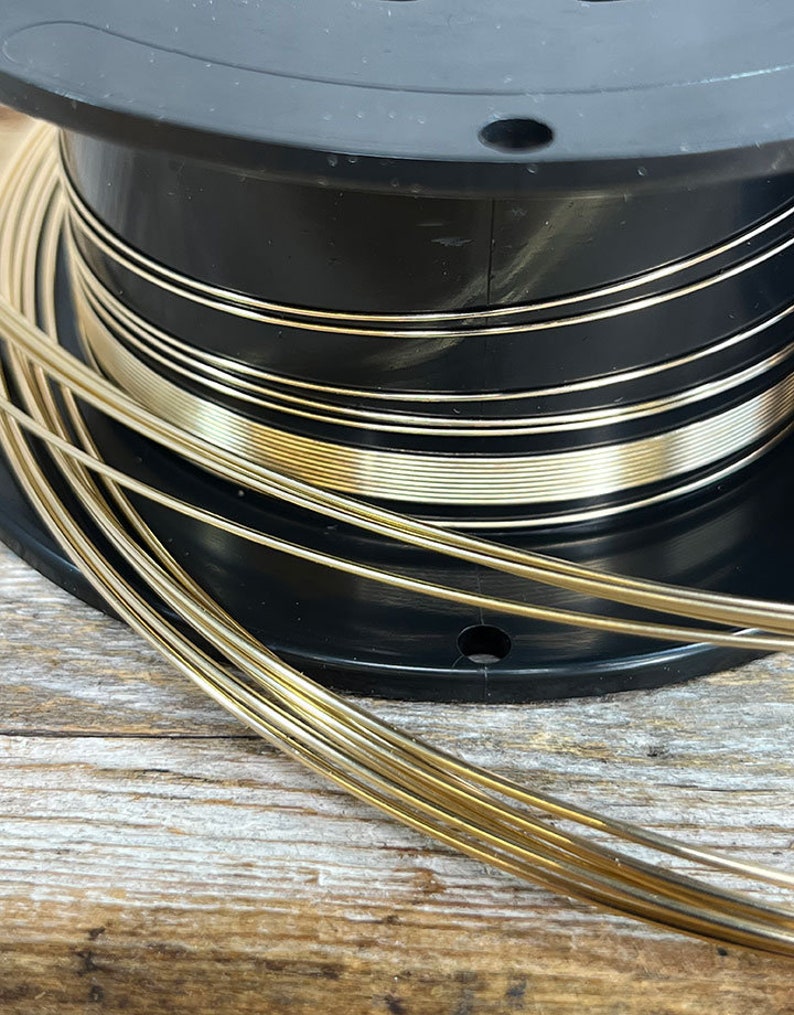 May include: A spool of gold-colored wire wound around a black plastic spool. The wire is thin and shiny.