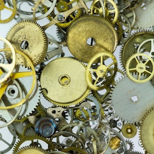 May include: A close-up of a collection of assorted gold and silver gears and clock parts. The gears are arranged in a random pattern, creating a visually interesting and intricate design.