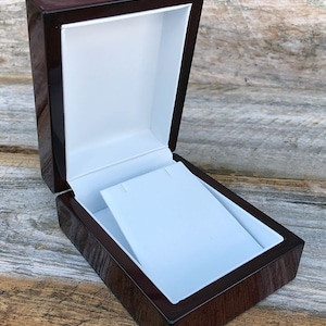 May include: A dark brown wooden box with a white velvet interior. The box is open and the velvet is folded to create a small platform for jewelry.