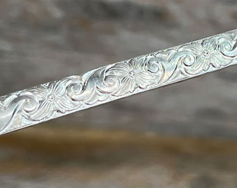May include: A silver bracelet with a floral design. The bracelet is engraved with a repeating pattern of flowers and leaves.