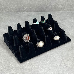 May include: Black velvet ring display with 20 slots for rings.  The display has seven rings on it, including a ring with a large, oval, red stone, a ring with a large, oval, white stone, and a ring with a turquoise stone.