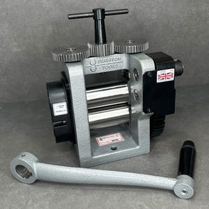 May include: A silver metal Durston Tools rolling mill with a black handle and gears. The mill has two rollers and a hand crank. The British flag is visible on the side of the mill.