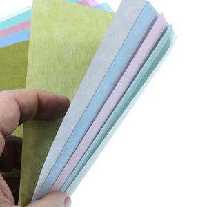 May include: A stack of colorful paper sheets in shades of green, blue, pink, and white. The paper is textured and has a slightly rough surface.