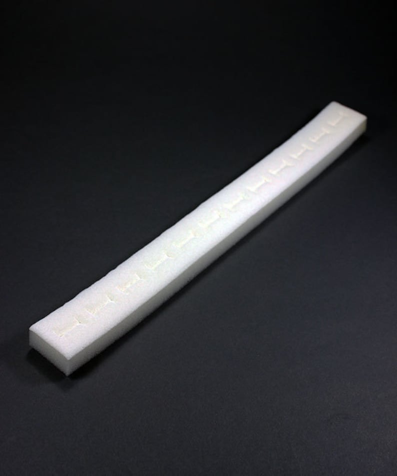 May include: A white foam strip with a series of evenly spaced holes running along its length. The strip is slightly curved and appears to be made of a soft, flexible material.