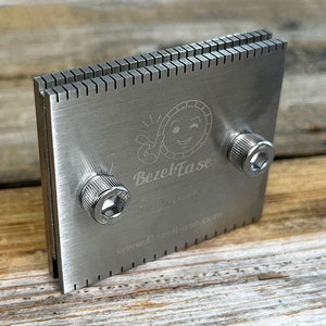 May include: A rectangular, stainless steel tool with a toothed edge and two hex screws. The tool has the text "BezelEase" and "PATENT PENDING" printed on it, along with the website address www.BezelEase.com.