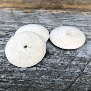 May include: Three white felt polishing wheels with a small hole in the center. The wheels are on a wooden surface.
