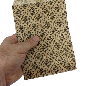May include: A brown paper bag with a black damask pattern. The bag is folded and held in a hand.