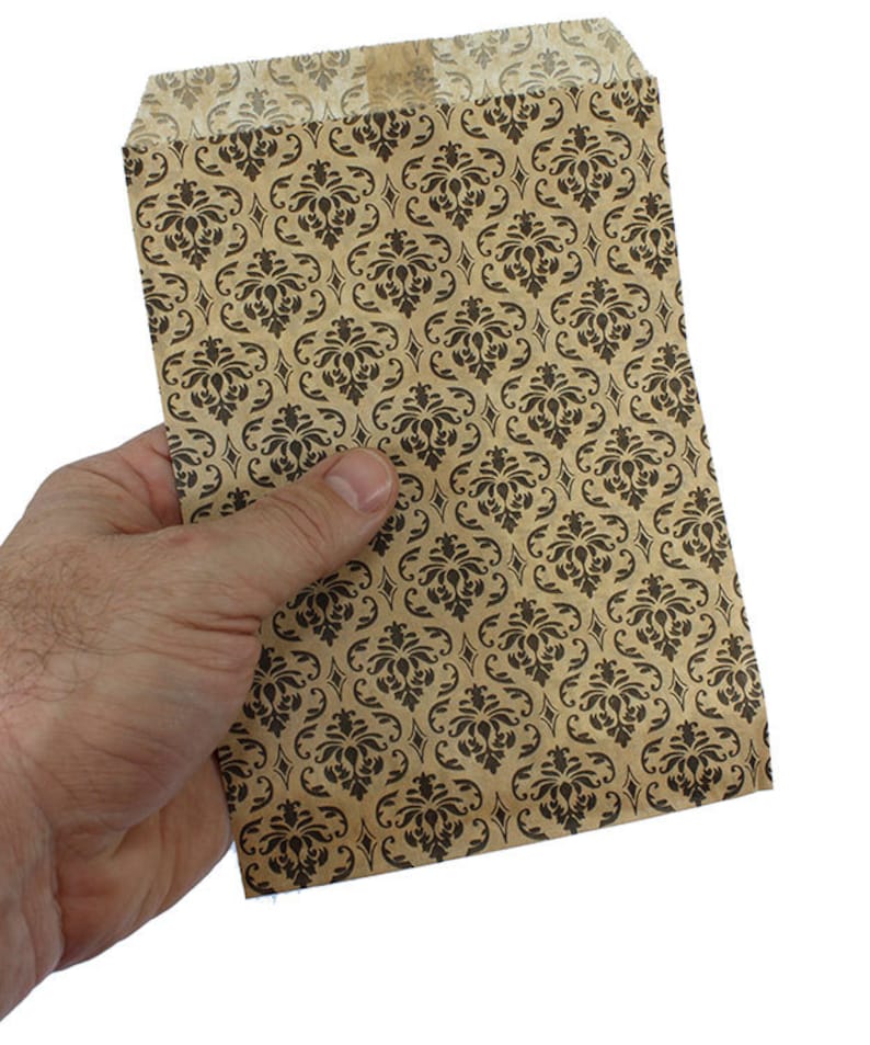 May include: A brown paper bag with a black damask pattern. The bag is folded and held in a hand.