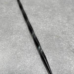 May include: A black, twisted metal tool with a pointed tip. It is a type of awl used for making holes in leather or other materials.