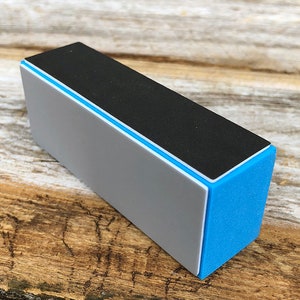 May include: A rectangular nail buffer with four sides. The top side is black, the next side is gray, and the bottom two sides are blue.