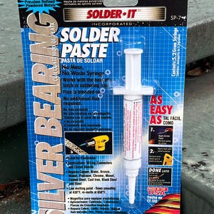 May include: Solder-It Silver Bearing Solder Paste in a syringe. The package is blue and white, with text in English and Spanish. The product is for electronics, with a low melting point of 430°F (221°C). Made in the USA.