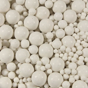 May include: A close-up image of a variety of white ceramic beads of different sizes. The beads are smooth and round, and they are arranged in a random pattern.