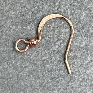 May include: A rose gold earring hook with a small ball at the top.
