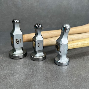 May include: Three silver metal hammers with wooden handles. The hammers have round heads and are labeled with the numbers "1129", "1121", and "1120".