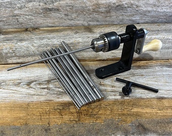 May include: A black metal drill press with a wooden handle and a set of 10 metal rods. The drill press is on a wooden surface.