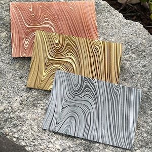 May include: Three marbled paper samples in different colors: copper, gold, and silver. The paper has a swirled pattern.