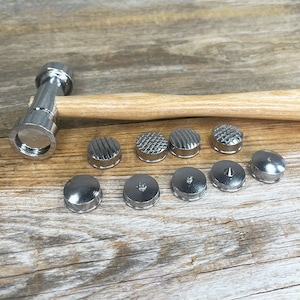 May include: A set of metal stamps for leather crafting, including a hammer with a wooden handle. The stamps feature various designs, including circles, squares, and triangles.