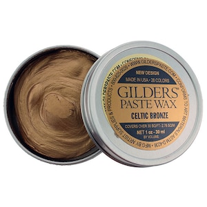 May include: An open, round metal tin of Gilders Paste Wax in Celtic Bronze. The bronze-colored paste is swirled inside the tin. The label reads "Gilders Paste Wax" and "Celtic Bronze". The tin is 1 oz - 30 ml.