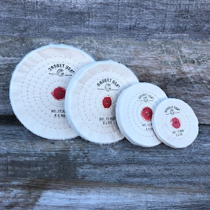 May include: Four white buffing wheels of different sizes with red centers and the text "GROBET USA" printed on them. The wheels are labeled with their size and number. The largest wheel is 6 inches in diameter, the next largest is 5 inches, the next is 4 inches, and the smallest is 3 inches.