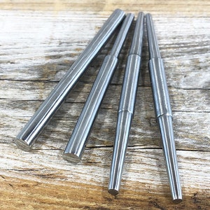 May include: Set of four silver metal mandrels, tapered and cylindrical, arranged in a fan shape on a wooden surface.