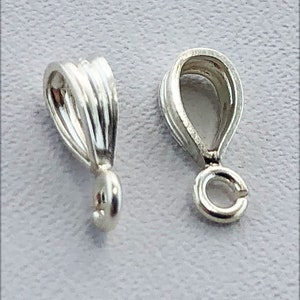 May include: Two silver-toned pendant bails with a loop at the bottom. The bails are designed with a decorative, ridged, teardrop shape.