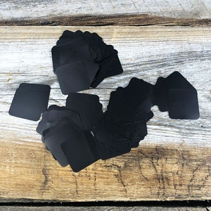 May include: A pile of black square plant markers on a wooden surface.