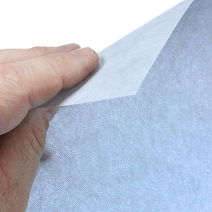 May include: A sheet of light blue textured paper with a slightly rough surface. The paper is being held by a hand, and the top edge of the paper is folded over.