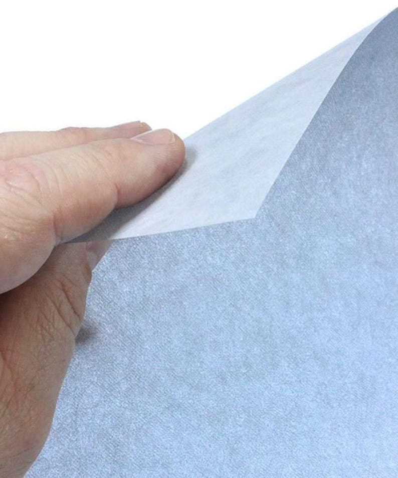 May include: A sheet of light blue textured paper with a slightly rough surface. The paper is being held by a hand, and the top edge of the paper is folded over.