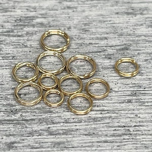May include: A collection of gold jump rings of various sizes, arranged on a wooden surface.