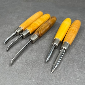 May include: Set of five wood handled carving tools with metal blades. The tools have different shaped blades for various carving techniques.