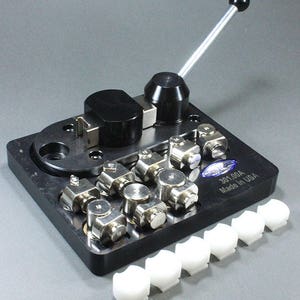 May include: A black metal tool with a lever and multiple silver metal pieces. The tool is labeled "301.00A Made in USA". There are seven white plastic pieces to the right of the tool.