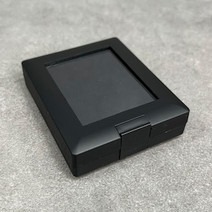 May include: A black rectangular box with a clear plastic window on the top. The box is closed and has a hinged lid.