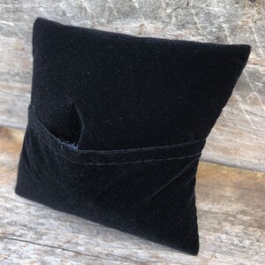May include: A black velvet pillow with a pocket on the front. The pillow is made of soft, plush fabric and is perfect for displaying small items.