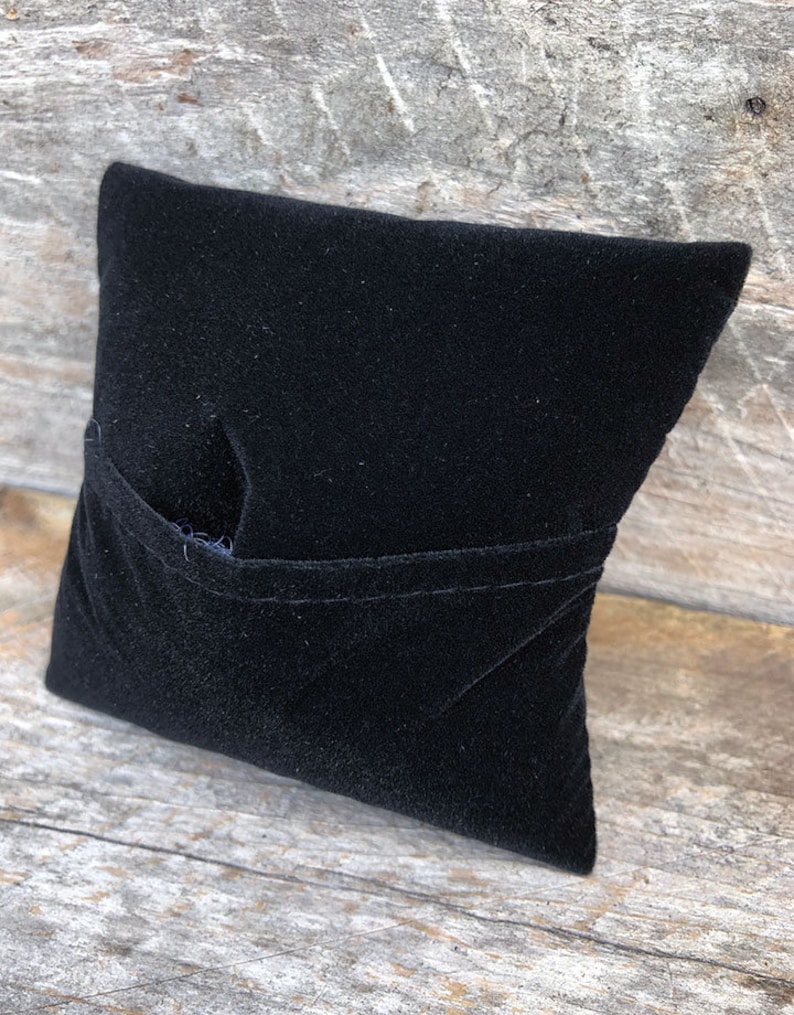 May include: A black velvet pillow with a pocket on the front. The pillow is made of soft, plush fabric and is perfect for displaying small items.