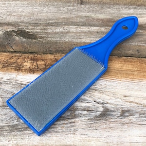 May include: A blue plastic brush with a gray bristle pad. The brush is designed for cleaning and polishing.