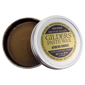 May include: A small tin of Gilders Paste Wax in the color African Bronze. The tin is open and the wax is visible inside. The label on the tin says "New Design" and "Made in USA - 28 Colors". It also says "Covers over 30 sq/ft - 2.78 sq m" and "Net 1 oz - 30 ml by volume".