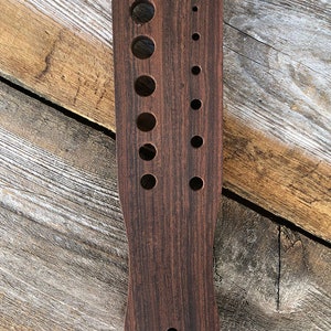 May include: A wooden tool with multiple round holes of varying sizes. The tool is dark brown and has a smooth, polished finish.