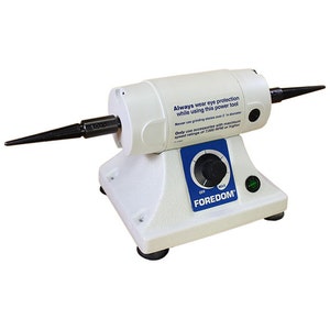 Może przedstawiać: Białe narzędzie elektryczne Foredom z czarną wrzecioną i pokrętłem regulacji prędkości. Narzędzie ma zieloną lampkę kontrolną i etykietę ostrzegawczą z napisem "Zawsze noś ochronę oczu podczas korzystania z tego narzędzia elektrycznego. Nigdy nie używaj kamieni szlifierskich o średnicy większej niż 2 cale. Używaj tylko akcesori&oacute;w o maksymalnej prędkości 7 000 obr./min lub wyższej."