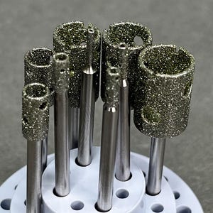 May include: A set of eight diamond-tipped drill bits in a white plastic holder. The drill bits are different sizes and have a silver finish.
