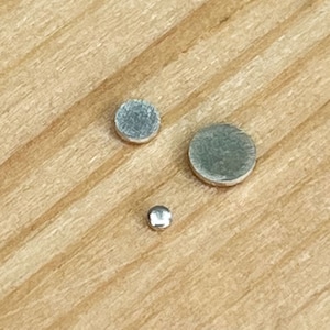 May include: Three silver metal discs of varying sizes on a wooden surface.