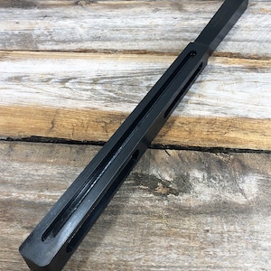 May include: A black metal bar with two long slots cut into it. The bar is about 12 inches long and 1 inch wide.