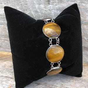 May include: A silver bracelet featuring three round tiger's eye stones. The stones are a rich brown colour with gold flecks.