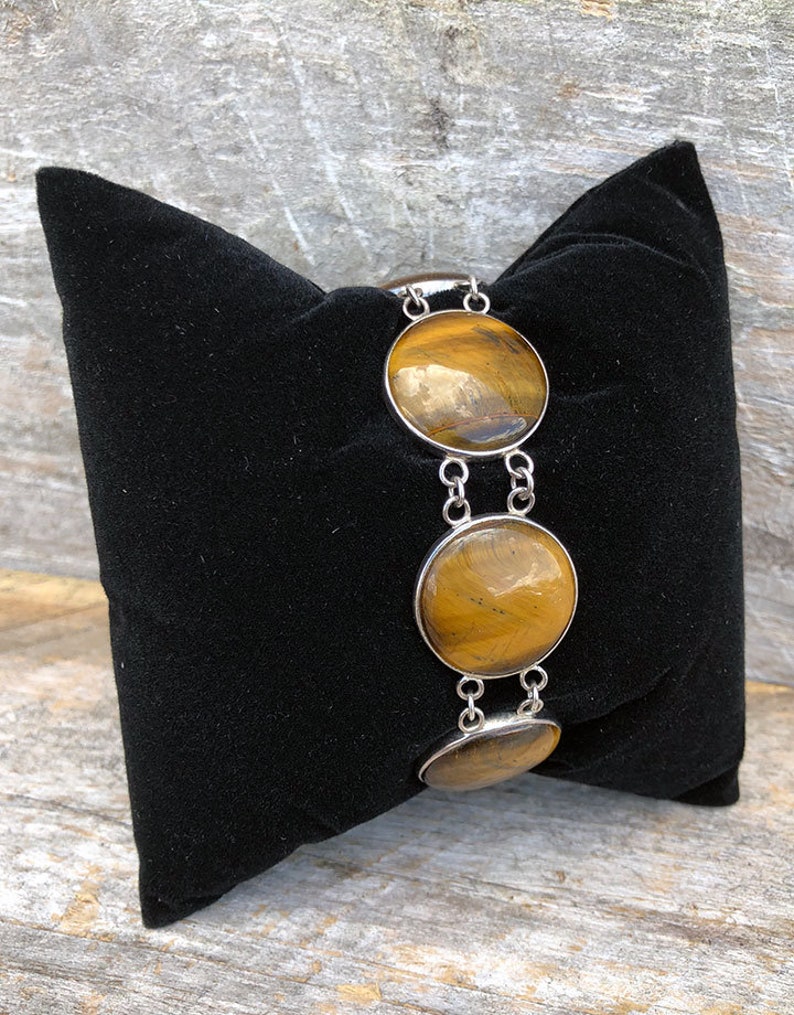 May include: A silver bracelet featuring three round tiger's eye stones. The stones are a rich brown colour with gold flecks.