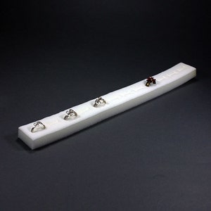May include: A white foam ring display with five rings. The rings are silver and have different designs. One ring has a red stone.