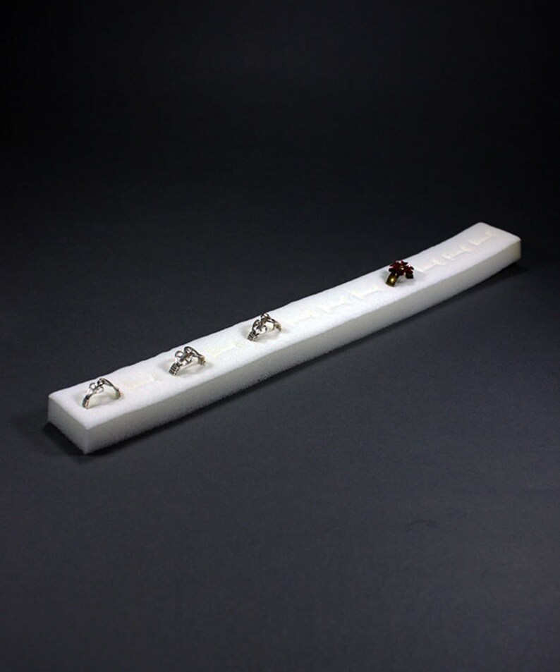 May include: A white foam ring display with five rings. The rings are silver and have different designs. One ring has a red stone.