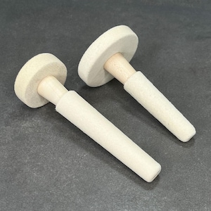 May include: Two white felt polishing tools with wooden handles. The tools are used for polishing jewelry or other small objects.