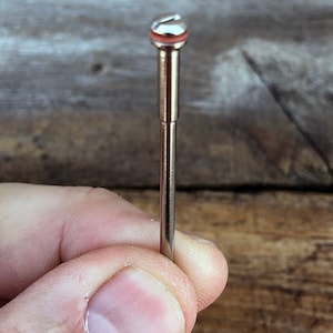 May include: A silver metal rotary burr with a red rubber band around the top. The burr is held in a hand.