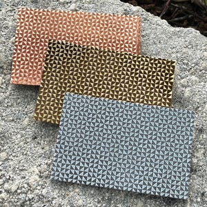 May include: Three rectangular pieces of fabric with a geometric pattern of small triangles. The fabric is in three colors: copper, gold, and gray.