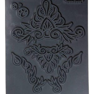 May include: A black rubber stamp with four intricate designs. The stamp features the text "Relaxed Grandeur" and "Chrishi Friessen".