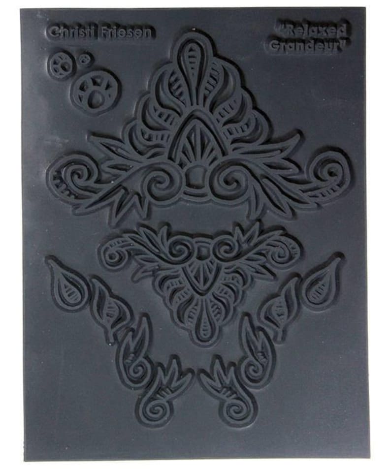 May include: A black rubber stamp with four intricate designs. The stamp features the text "Relaxed Grandeur" and "Chrishi Friessen".